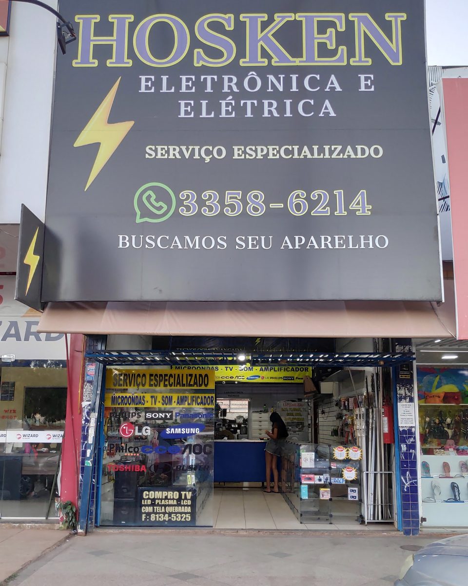 Fachada da Hosken Eletrônica e Elétrica: letreiro preto com letras azuis, raio amarelo e a frase buscamos seu aparelho